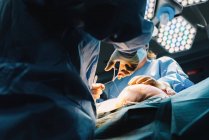 Dal basso chirurgo plastico che cuce il seno di paziente femminile dopo aver inserito impianti in sala operatoria — Foto stock