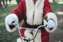 Неузнаваемый человек в костюме Санта-Клауса сидит на велосипеде и звонит в колокол — стоковое фото