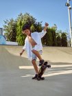 Niño feliz con casco protector y monopatín en rampa en skatepark - foto de stock