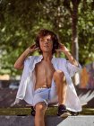 Menino pensativo casual em fones de ouvido sentado no skate enquanto relaxa no parque de skate no verão ensolarado durante o dia e olhando para longe — Fotografia de Stock