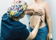 Back view of female medic drawing markings on body of naked woman for breast surgery in clinic — Stock Photo