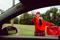 Молода жінка в червоному светрі жестикулює біля машини на дорозі — стокове фото
