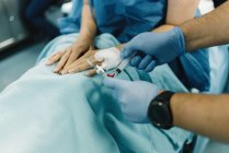 Paciente do sexo feminino em cultura, sentada com as pernas cobertas e agulha de fluido intravenoso na mão antes da cirurgia na sala de cirurgia — Fotografia de Stock