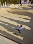 Vista de cima de criança em capacete que se deita com olhos fechados e gelando no chão em skatepark com sombras — Fotografia de Stock