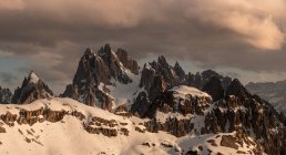 Paysage majestueux de sommets rocheux enneigés sous de lourds nuages sombres dans un ciel gris à Dolomites, Italie — Photo de stock
