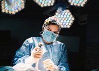 De baixo grave jovem médico em máscara protetora e cap fazendo cirurgia com instrumentos e enfermeira cultura — Fotografia de Stock