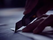 Руки профессионального человека, режущего листы бумаги специальным острым ножом на рабочем столе — стоковое фото