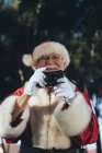 Sorridente uomo anziano in costume di Babbo Natale in piedi e scattare foto con macchina fotografica su sfondo naturale — Foto stock