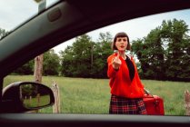 Mujer joven en suéter rojo gesticulando cerca de coche en la carretera - foto de stock