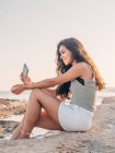Sonhador moda jovem mulher mensagens de texto na praia — Fotografia de Stock