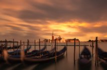 Anlegestelle mit leeren Booten im Wasser gegen den feurigen Sonnenuntergang und Stadt mit alten Türmen und Dächern — Stockfoto