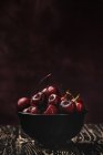Tasty appetizing ripe cherries in bowl on wooden table on dark background — Stock Photo
