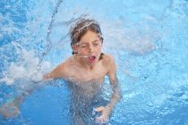 Captación de niños para el aire con los ojos cerrados y la boca abierta mientras flotan bajo cascada en el parque acuático. - foto de stock