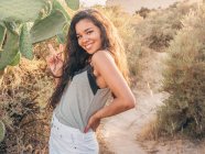 Sorridente allegra donna casual in piedi accanto a cactus sul sentiero sabbioso — Foto stock