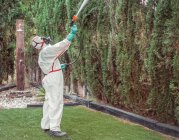 Фумигатор в белой униформе, распыляющий вещество в саду — стоковое фото