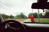 Женщина в красном свитере ловит машину на дороге в сельской местности — стоковое фото