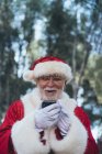 Веселый человек в костюме Санта-Клауса с помощью современного мобильного телефона на размытом фоне природы — стоковое фото