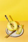 Taglio maturo appetitoso dolce melone snocciolato su piatto con cucchiaio e forchetta su fondo giallo e arancio — Foto stock