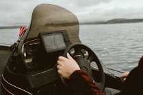 Faceless person holding steering wheel of boat sailing along route constructed using navigator in bad cloudy weather — Stock Photo