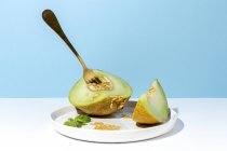 Corte maduro apetitoso doce melão sem caroço no prato com colher e garfo no fundo azul — Fotografia de Stock