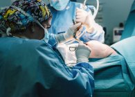 Вид збоку серйозного молодого лікаря в захисній масці та операції на шапочці з інструментами та медсестрою врожаю — стокове фото