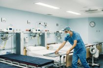 Sanitäter in blauer Uniform und Schutzmaske stellen Tablett auf Trolley im Krankenhauszimmer vor leeren Betten auf — Stockfoto