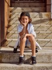 Menino pensativo sentado no skate nas escadas no parque de skate no verão ensolarado olhando na câmera — Fotografia de Stock