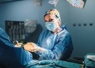 Доктор в хірургічній сукні тримає підготовлений силіконовий імплантат для мамопластики та медичної сестри під час операції — стокове фото