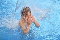 Bambino che aspira per aria con gli occhi chiusi e bocca aperta mentre galleggia sotto la cascata nel parco acquatico — Foto stock