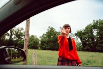 Young woman in red sweater gesturing near car on road — Stock Photo