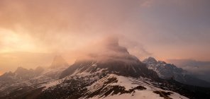 Montagna misteriosa con vetta innevata nella foschia nebbiosa contro il cielo del tramonto nelle Dolomiti — Foto stock