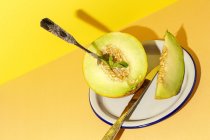 Taglio maturo appetitoso dolce melone snocciolato su piatto con cucchiaio e forchetta su fondo giallo e arancio — Foto stock
