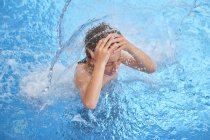 Kind schnappt nach Luft mit geschlossenen Augen und offenem Mund, während es unter Wasserfall im Wasserpark schwebt — Stockfoto
