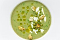 Зверху пюре з овочево-вершкового супу з зеленим горохом і дрібними крекерами на білому тлі — стокове фото