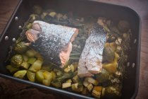 From above roasting pan with large pieces of salmon with skin on garnish of assorted baked vegetables and greens — Stock Photo
