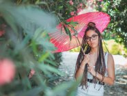 Nachdenkliche junge Frau im Sommeroutfit mit Regenschirm steht im Park — Stockfoto