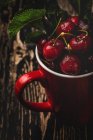 Смачні апетитні стиглі вишні з листям у червоній чашці на темному дерев'яному столі — стокове фото