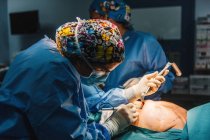 Seitenansicht des Arztes im Chirurgenkittel und Schutzmaske schneidet Brust einer Patientin, die auf dem Bett liegt — Stockfoto