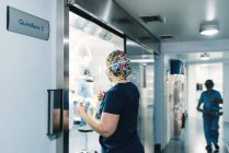 Vista lateral de la mujer en uniforme azul y máscara protectora que viene en el quirófano y enfermera caminando a lo largo del pasillo - foto de stock