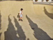 D'en haut heureux petit garçon portant casque de protection et planche à roulettes d'équitation sur la rampe dans skatepark — Photo de stock