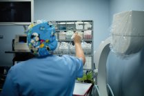 Обратный вид женщины-медика в синей форме, принимающей необходимые для операции материалы в больнице — стоковое фото