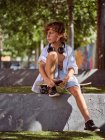 Casual menino pensativo em fones de ouvido usando telefone celular sentado no skate — Fotografia de Stock