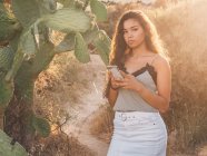 Juguetona mujer joven de moda mensajes de texto en el campo desierto - foto de stock