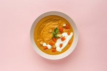 Сверху вкусный ароматный апельсиновый крем-суп с нарезанной морковью и пармезаном в белой миске на розовом фоне — стоковое фото