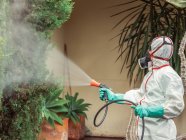 Fumigator in white uniform spraying substance on garden — Stock Photo