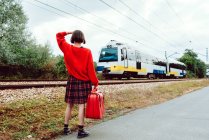 Женщина с чемоданом идет по железнодорожным путям и смотрит на расстояние — стоковое фото