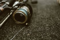 Fishing rod with shiny fishing reel with black cover and blue strong line for fishing on pebble — Stock Photo