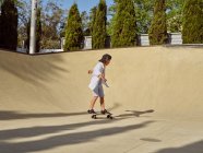 Счастливый маленький мальчик в защитном шлеме и на скейтборде на рампе в скейтпарке — стоковое фото