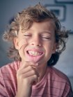 Неустойчивый детский зуб в широко открытом рту анонимного ребенка, тянущего губу вниз, чтобы показать зуб с закрытыми глазами — стоковое фото