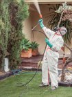 Begaser in weißer Uniform sprüht Substanz auf Garten — Stockfoto